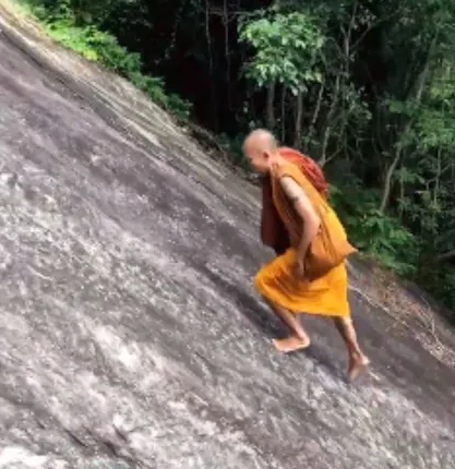 Monk climbs up a steep mountain without a safety harness